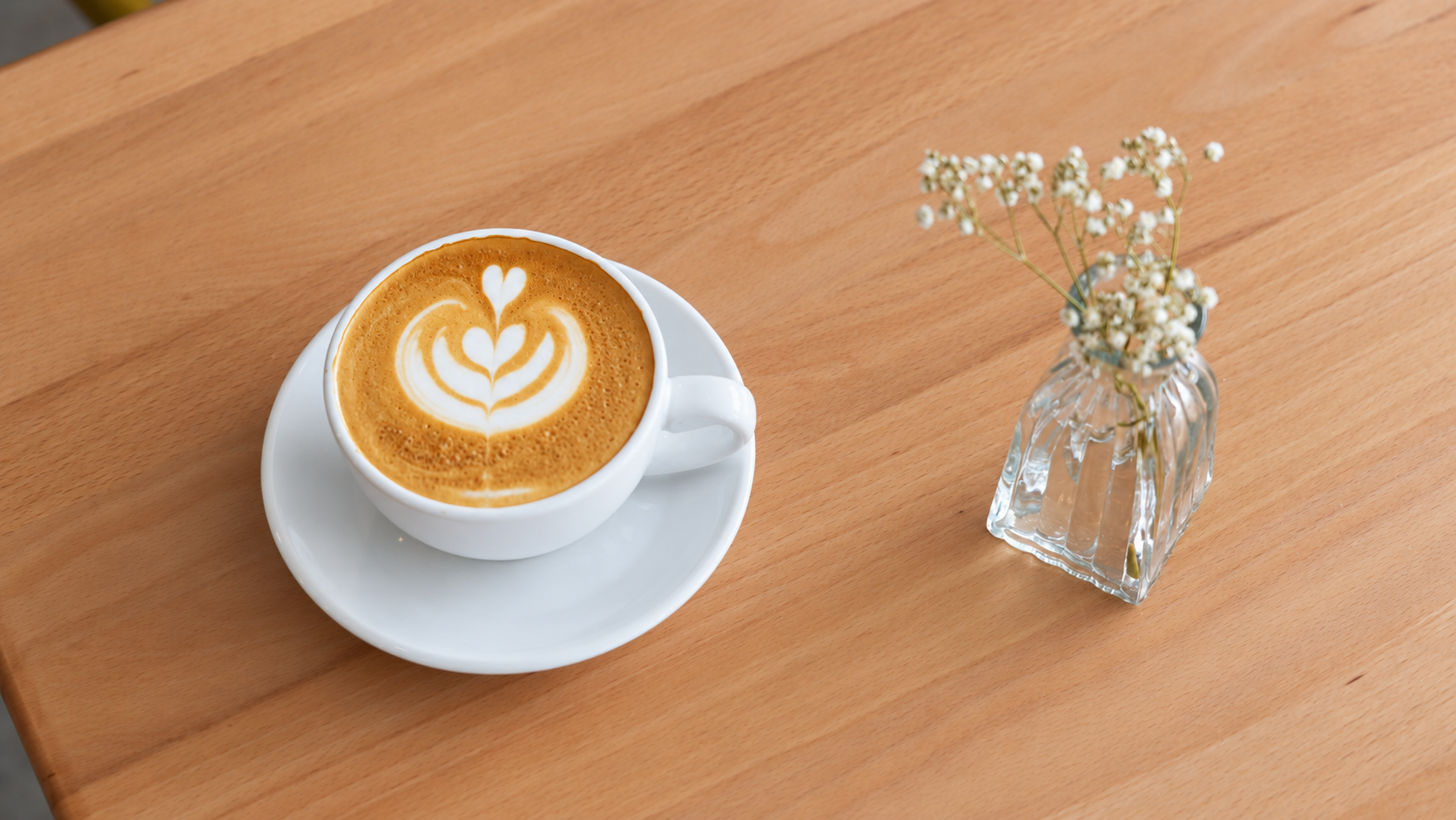 Latte art in a white cup beside flowers on a Le Brulée café table