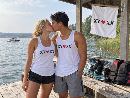Young adult couple kissing in matching white TSF tank tops at a wakeboarding dock.