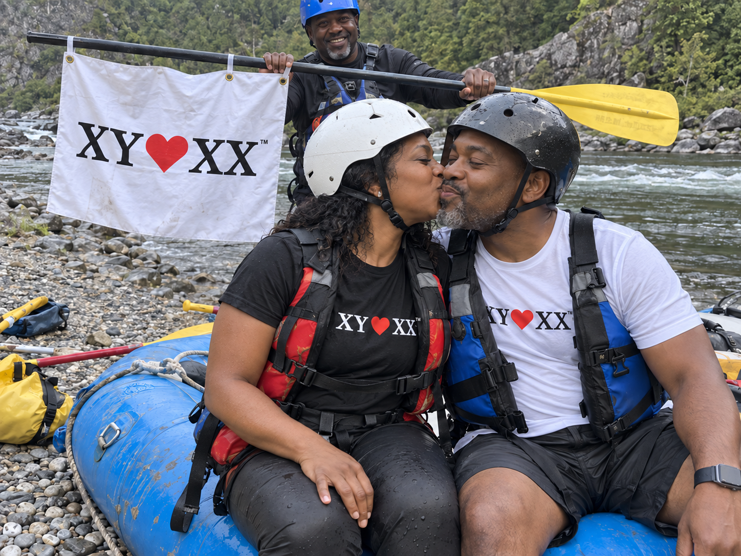 Couple in rafting gear sharing a kiss beside a raft with a flag hanging from a paddle.