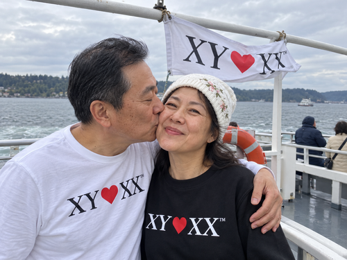 Older couple sharing a cheek kiss aboard a ferry beneath a naturally folded flag.