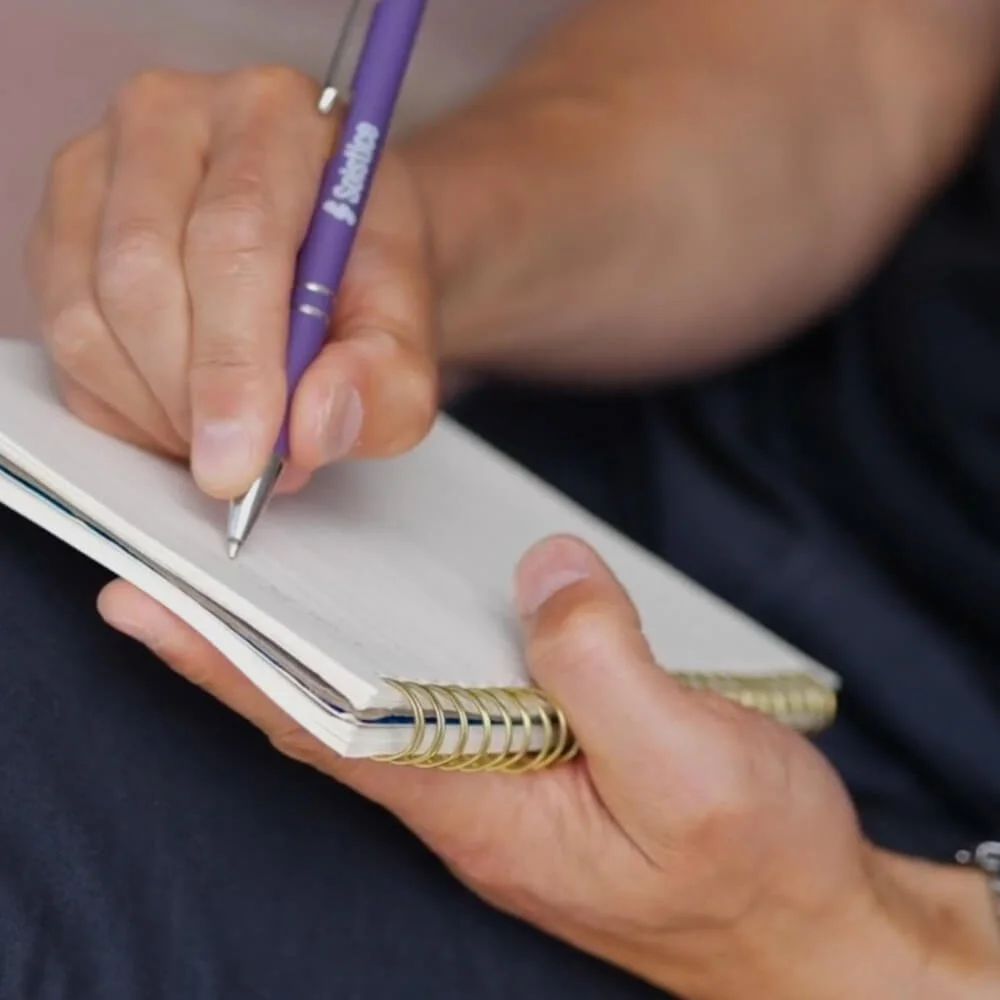 A hand writing with a purple pen in a notebook. The text reads 'Deep work'