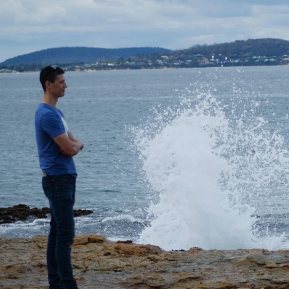 Daniel looking out onto the ocean, as waves crash in the background. Text reads 'Saying yes'