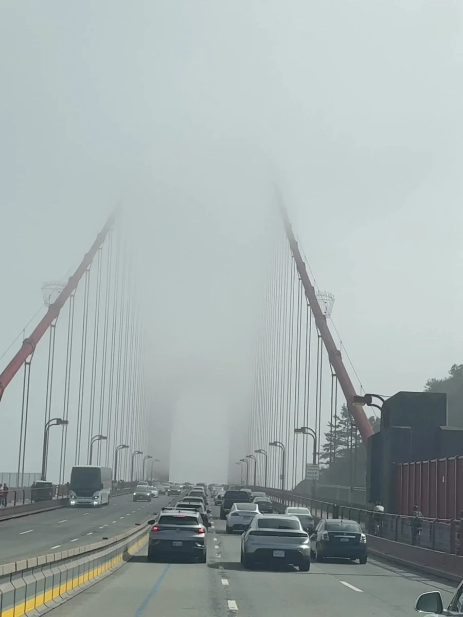 Driving across the Golden Gate Bridge in fog, its orange towers fading into the cloud
