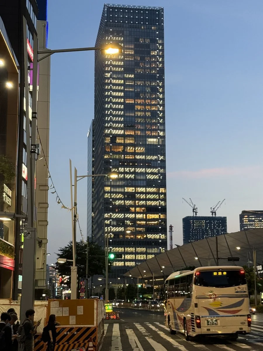 A Tokyo street at dusk, with a tall office tower and a bus at the crossing