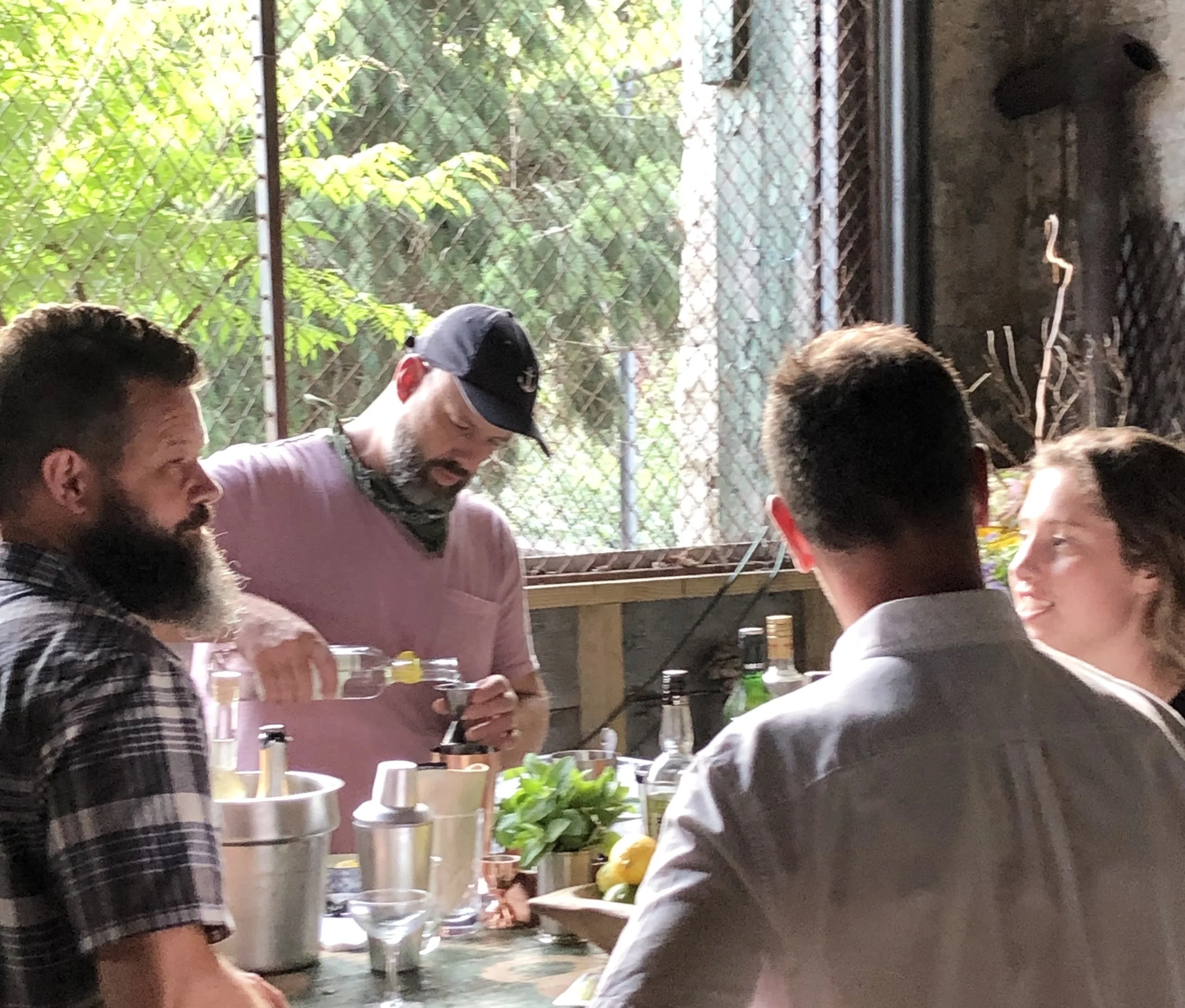 People gathering around a table while drinks are prepared.