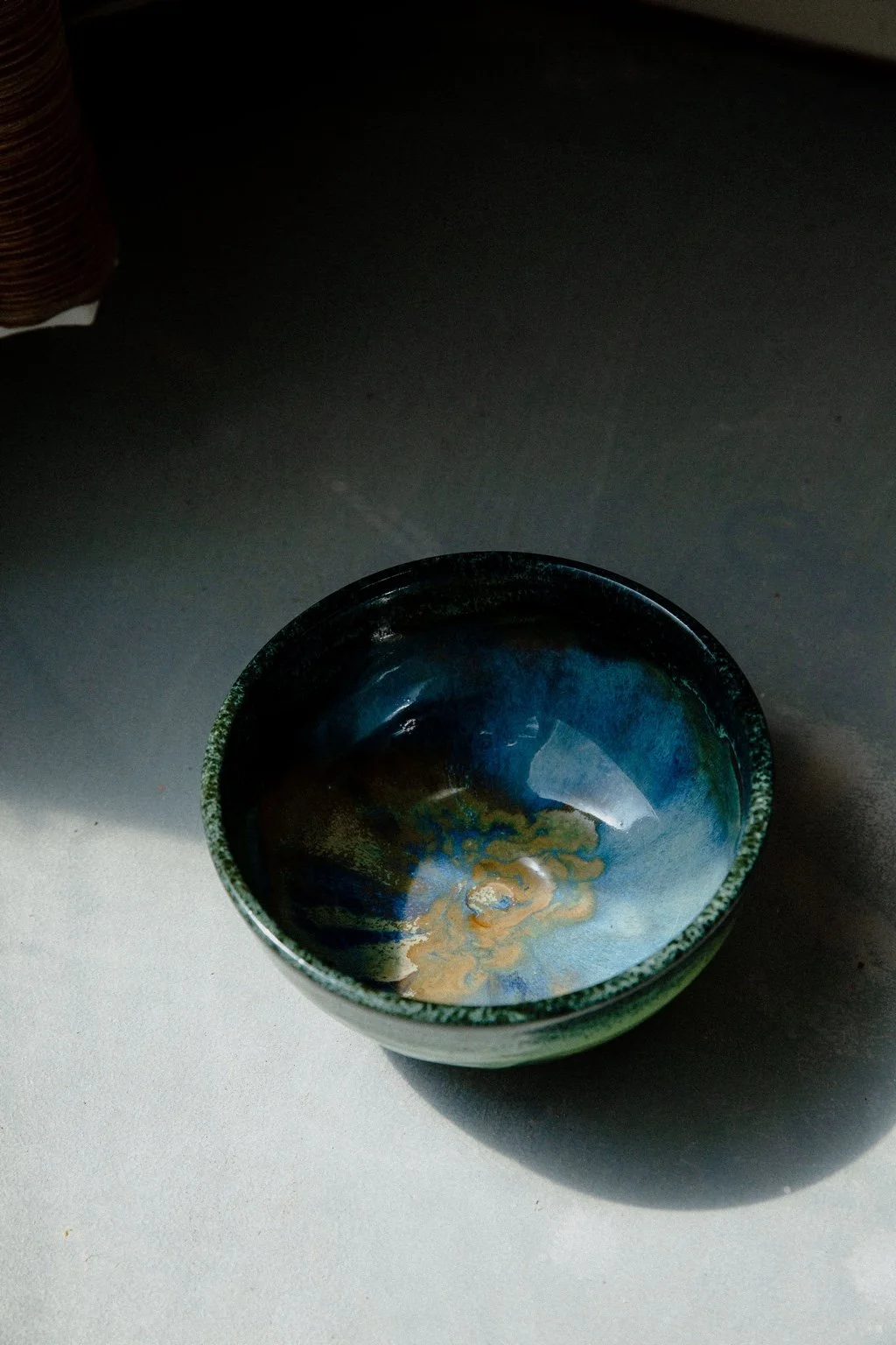 A handmade blue bowl with flowing gold and green glaze in natural light