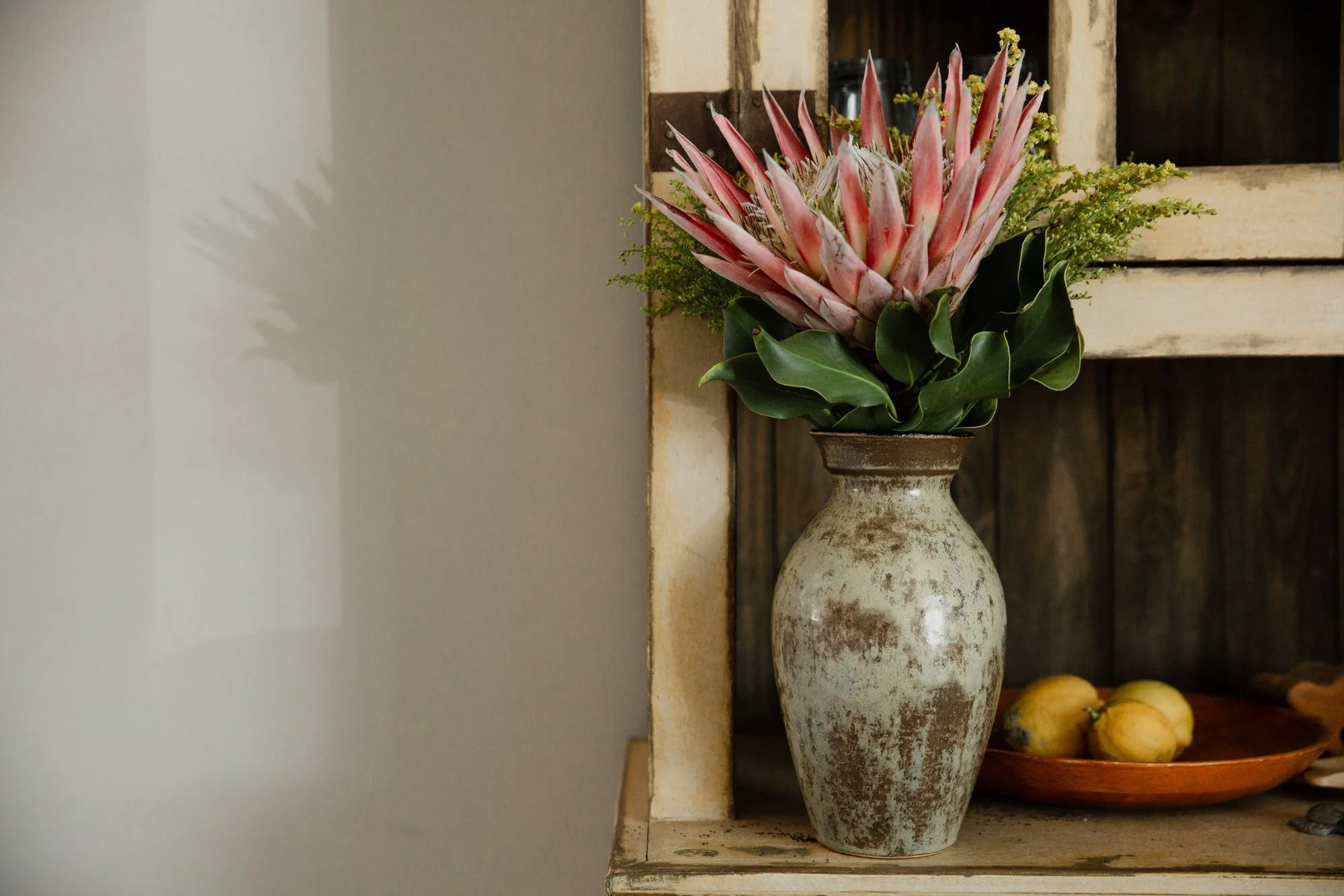 A handmade vase holding flowers, beside a serving dish of lemons
