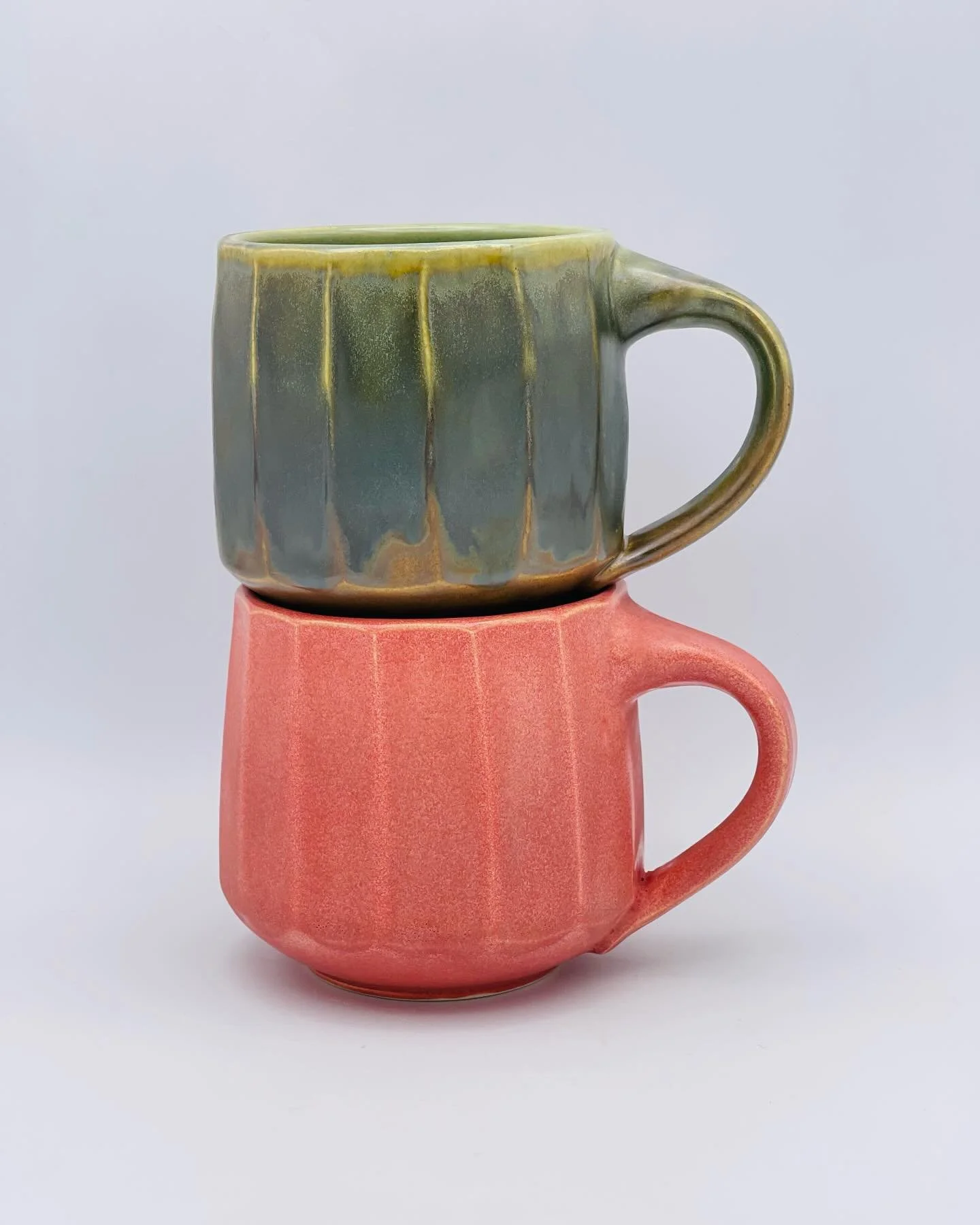 Two stacked handmade mugs in green and coral glazes