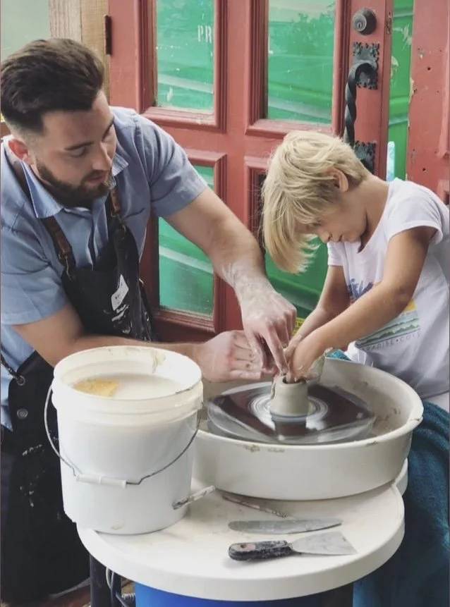 John helping a young student shape clay on the pottery wheel