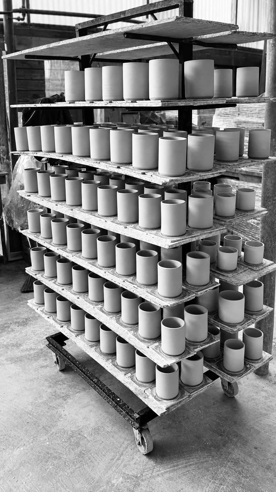 Black and white photograph of handmade ceramic vessels drying on a studio rack