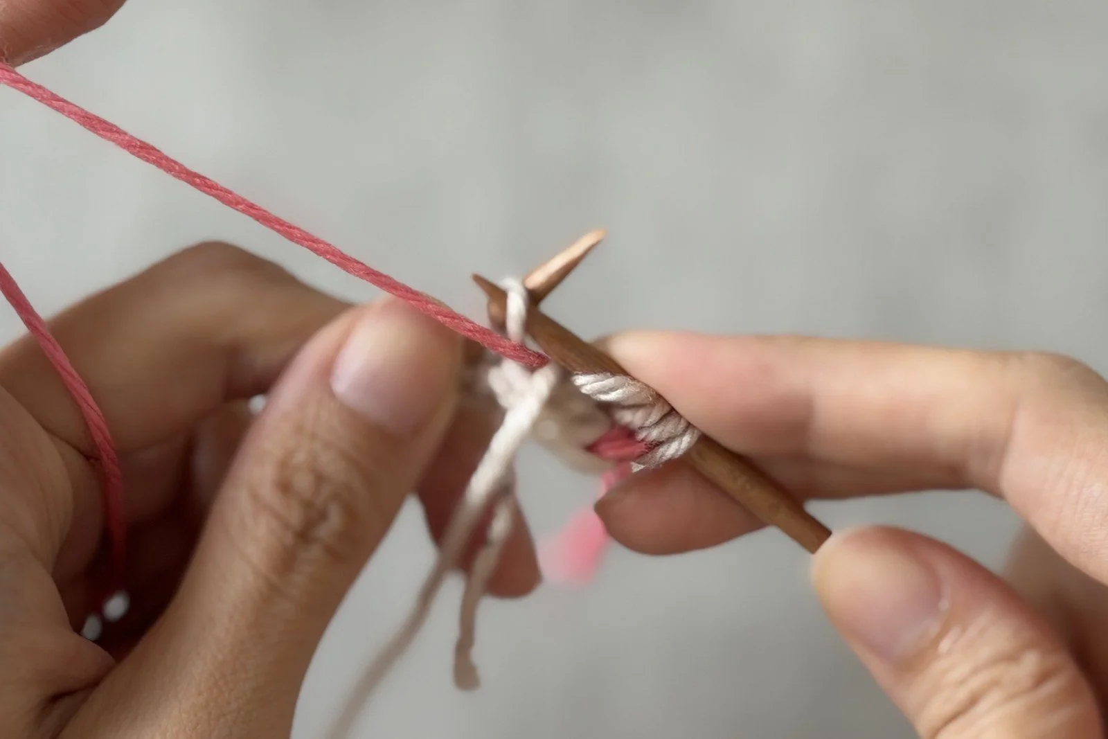 Pink MC being brought through the lifted strand in a purl stitch.