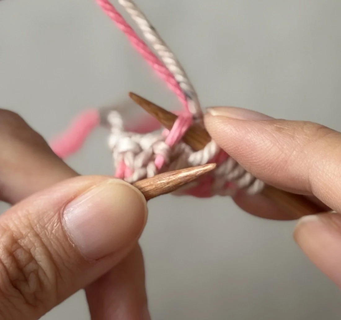 Close-up: Both working yarns in front while the pink MC bar is lifted for the second increase.