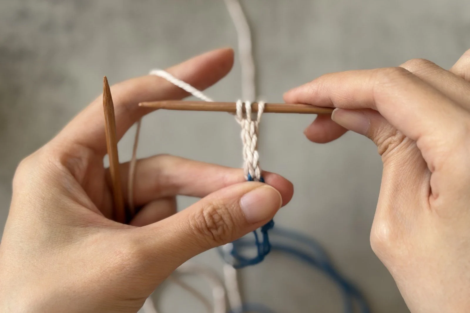 A short white I-cord tab hanging below three live stitches on the needle.