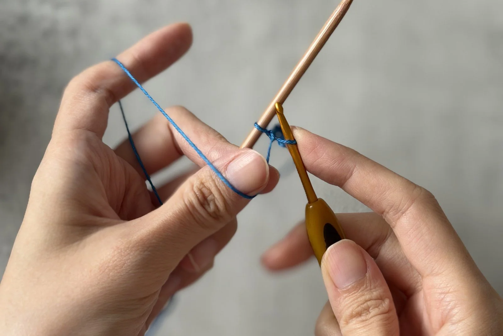 Blue waste yarn passing over the wooden needle beside the crochet hook.