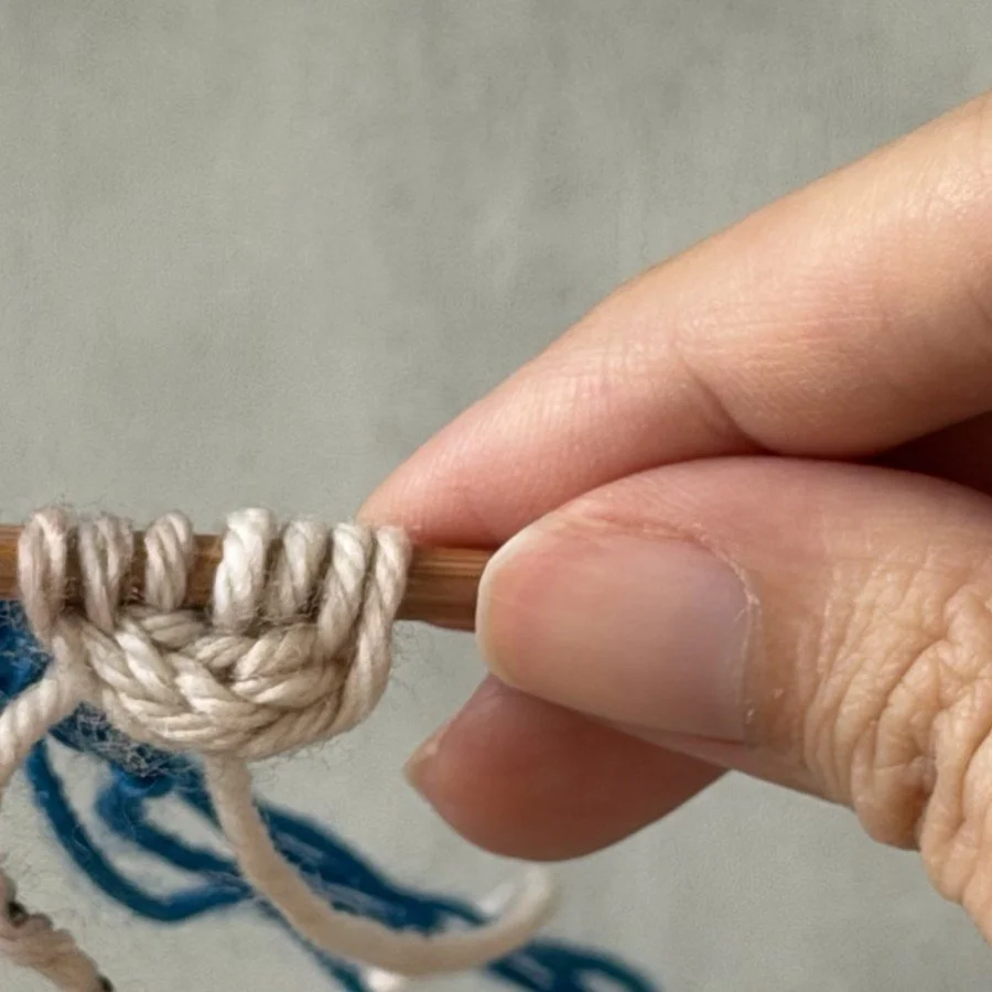 Close-up of the three recovered white stitches supported on the needle above the blue chain.