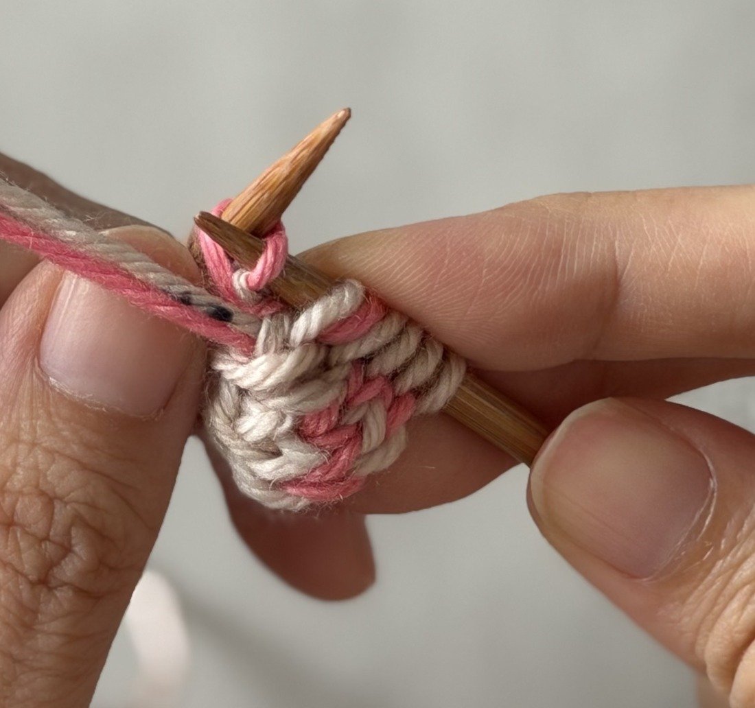 Close-up: Pink MC yarn used to purl through the back loop of the lifted bar.