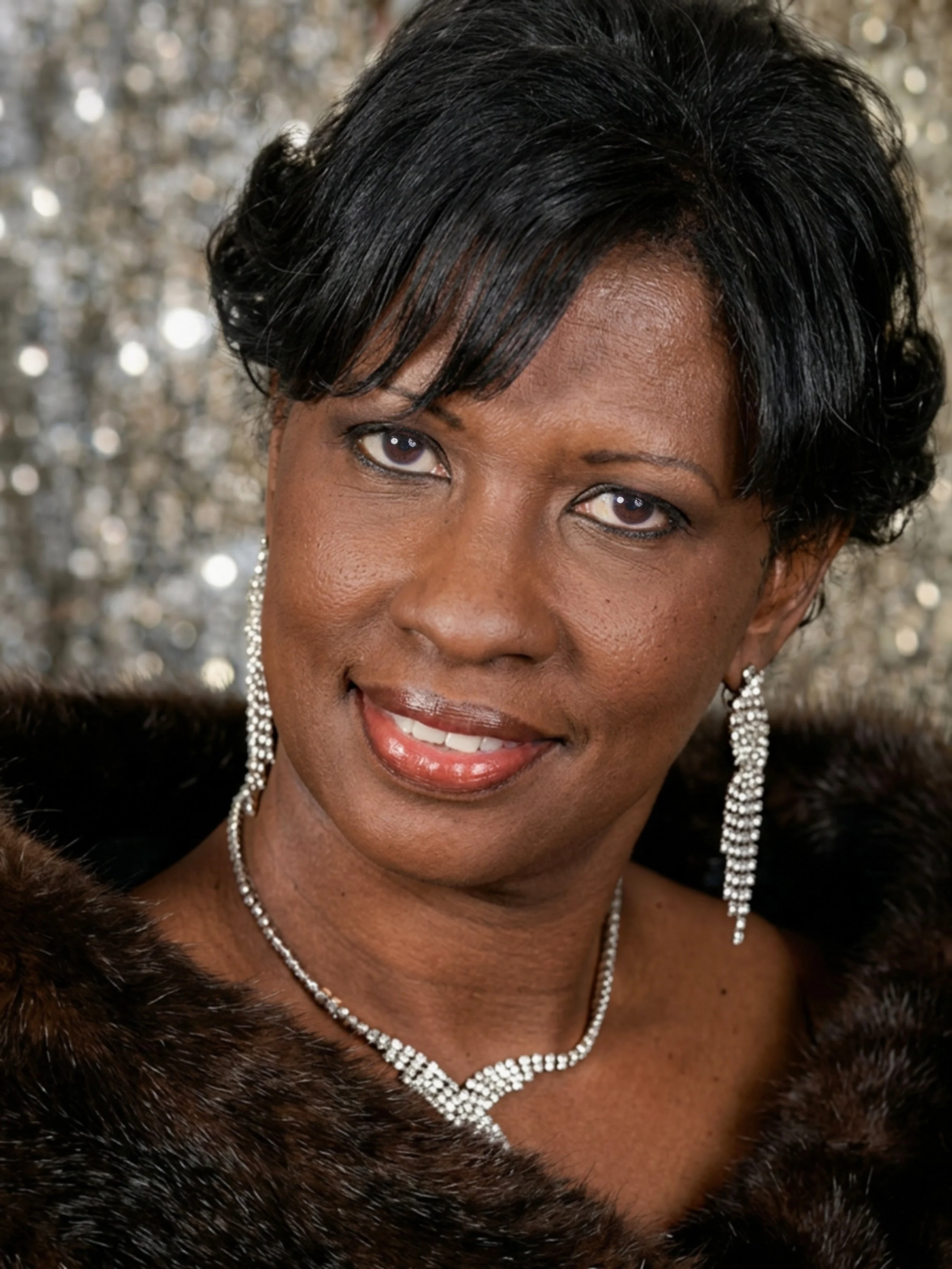 Ophelia Holmes, in a black dress with silver jewelry, in front of a sequined backdrop