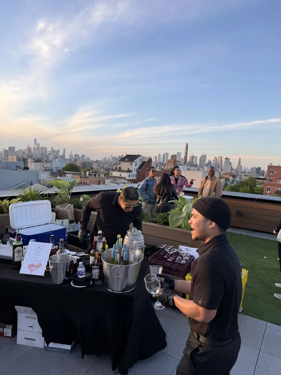 Two bartenders working at an outdoor bar with the city skyline behind them.