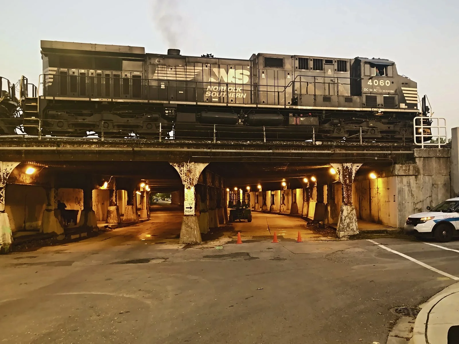 Freight locomotive crossing a rail viaduct above a lit underpass at dusk