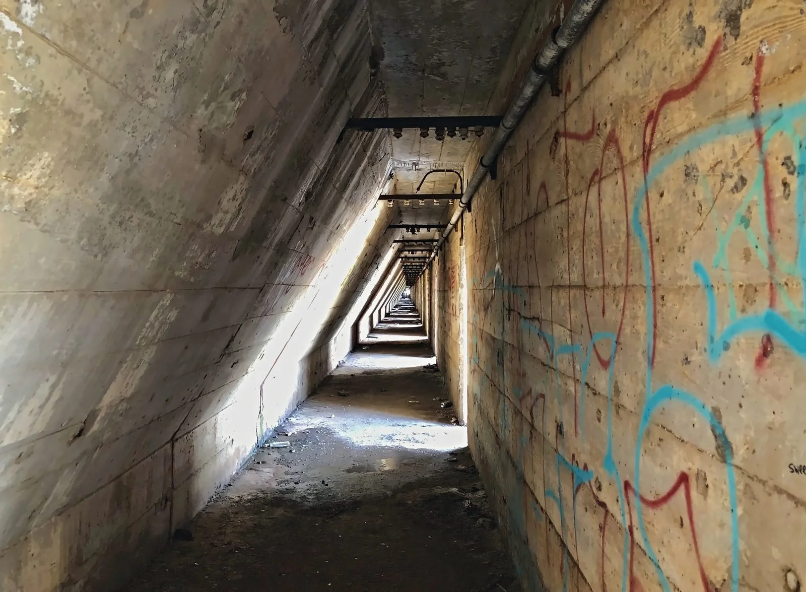 Long concrete tunnel inside an industrial wall, with sunlight raking across the floor