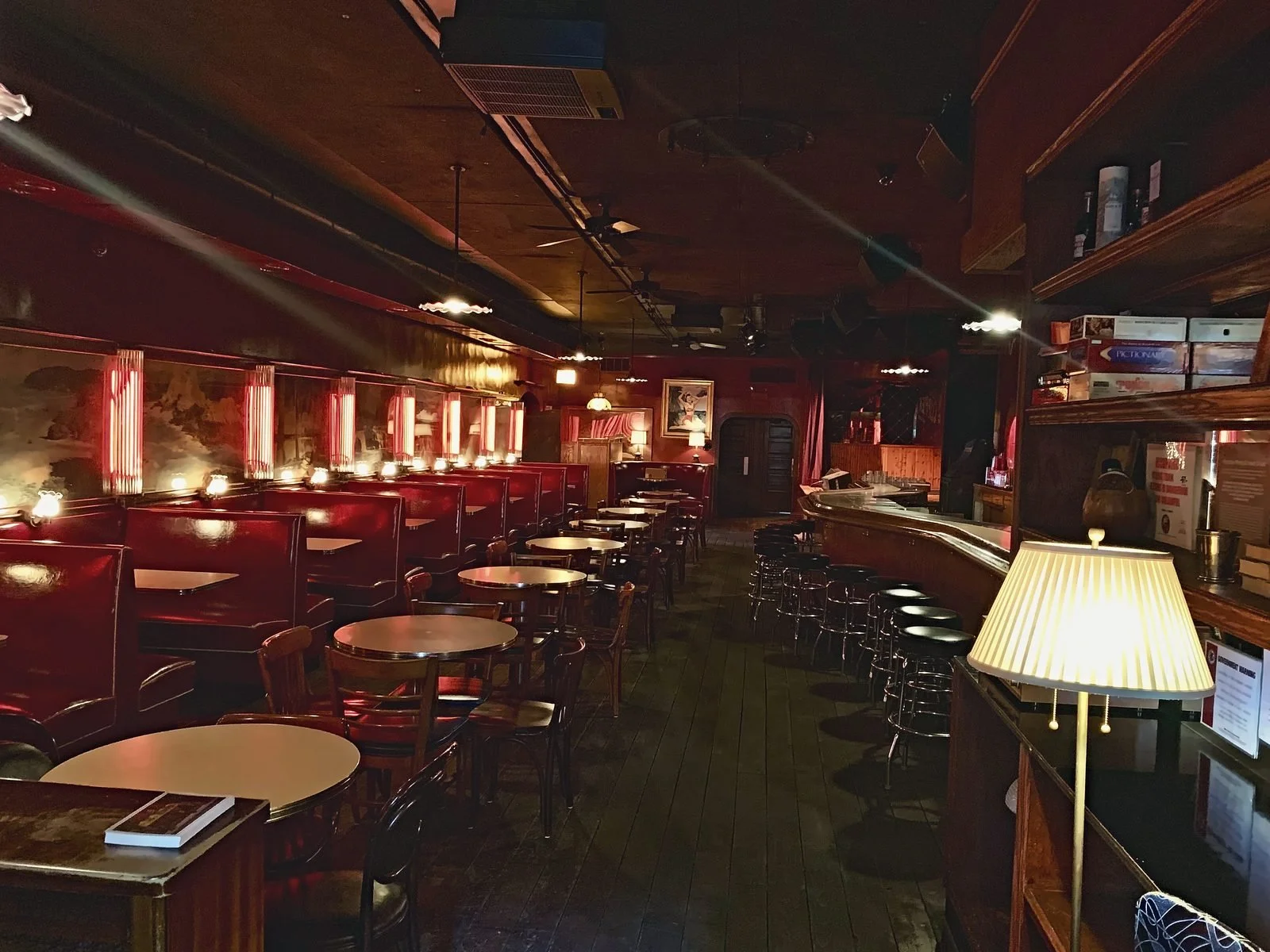 Dim vintage lounge with red leather booths, round tables and a long bar