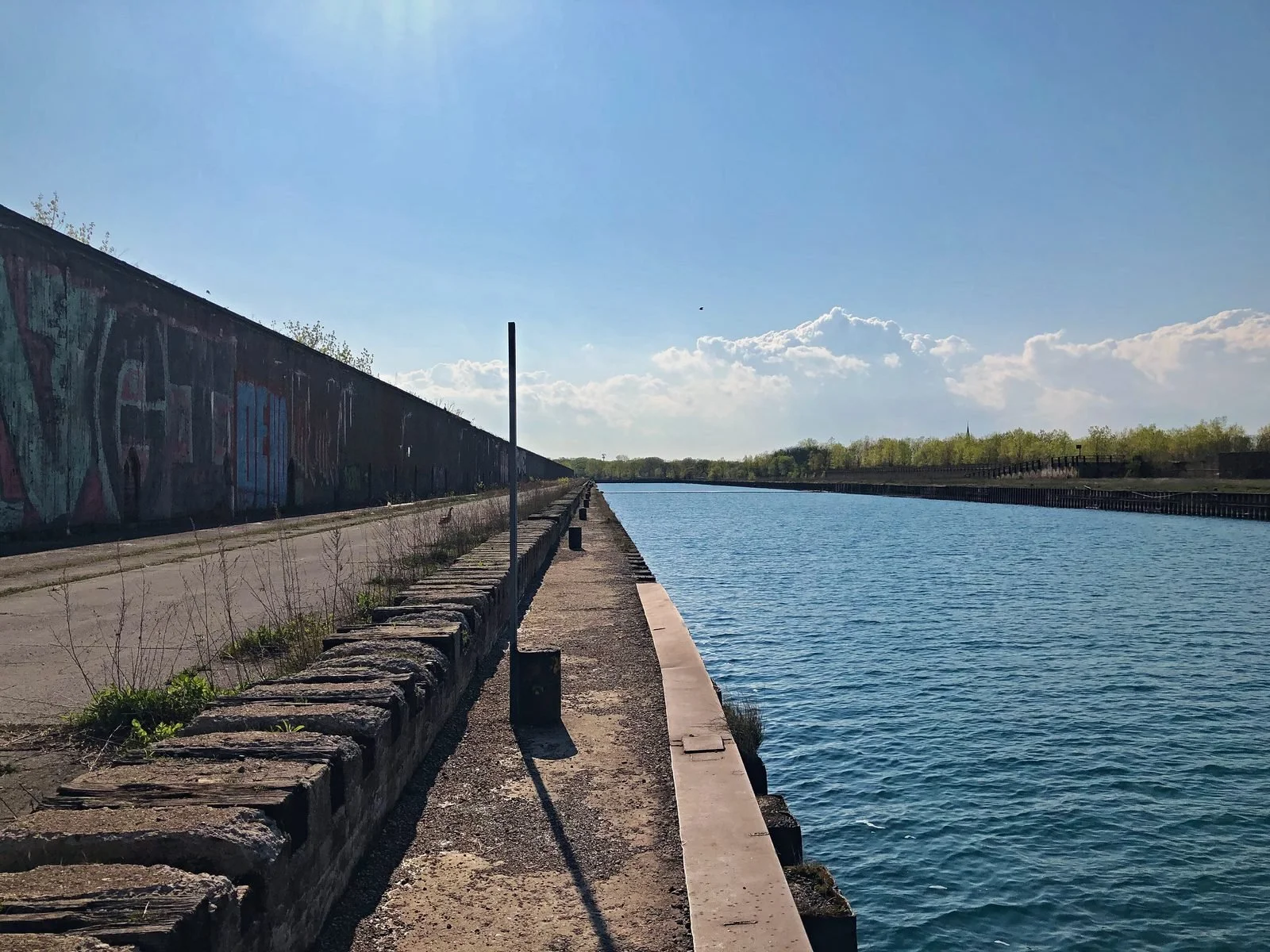 Concrete pier walk beside a long industrial wall and a calm blue water slip