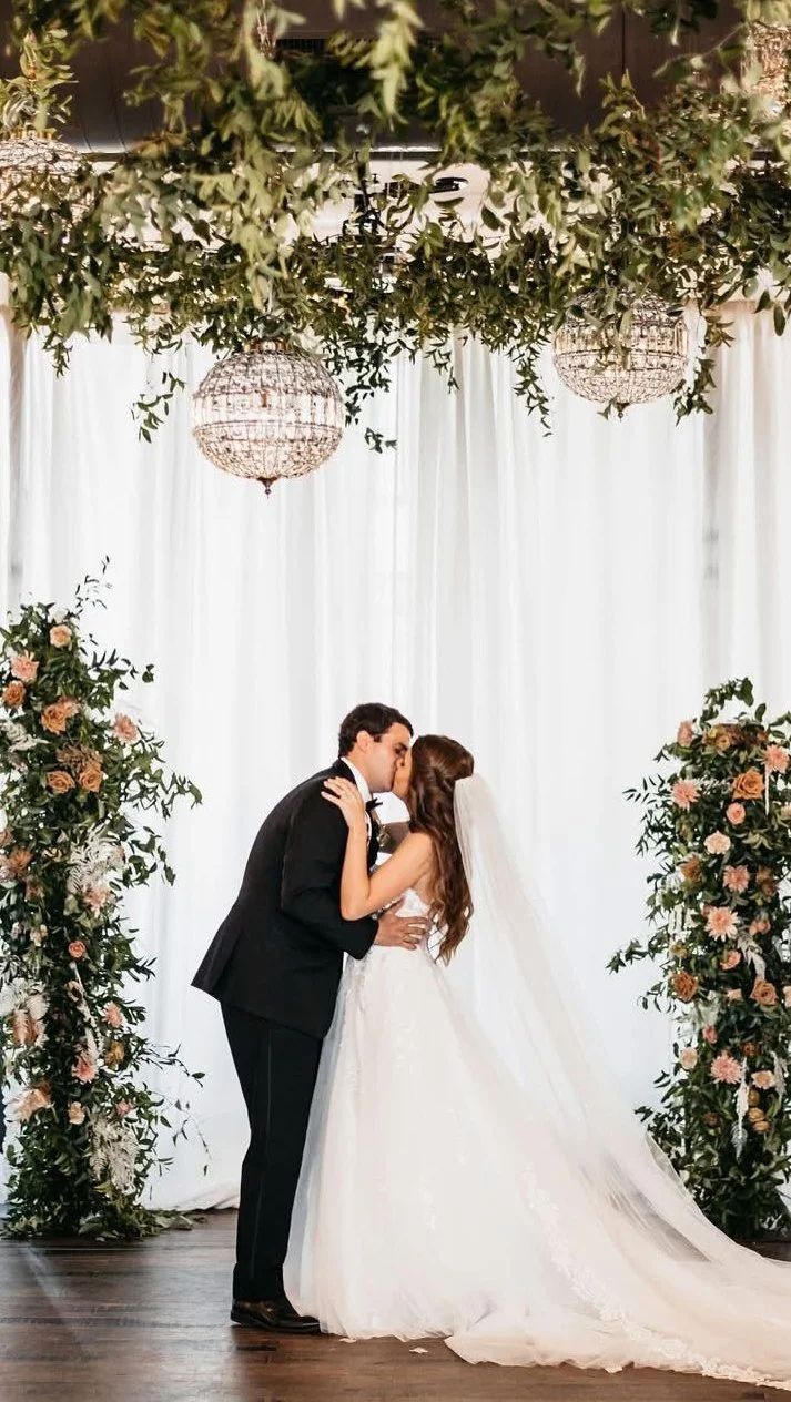 Newlyweds kissing beneath greenery and crystal chandeliers
