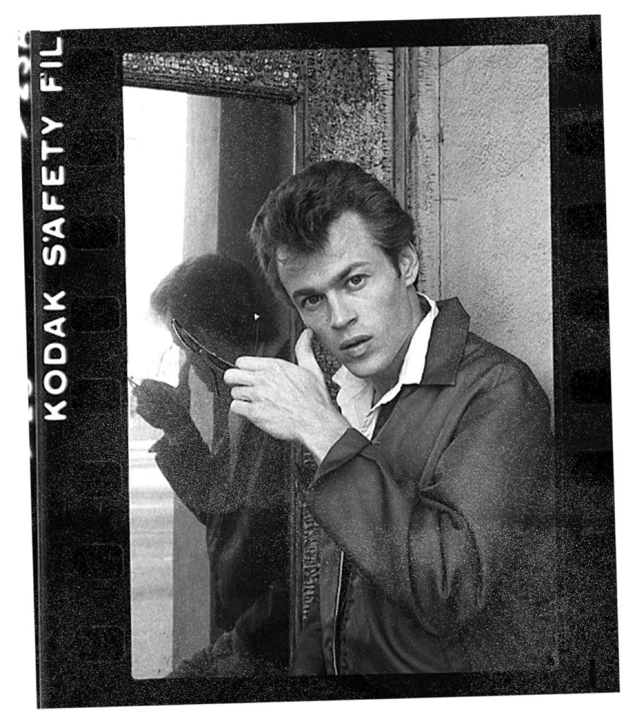 Jack Lee photographed on 35mm film, holding sunglasses, reflected in a doorway mirror