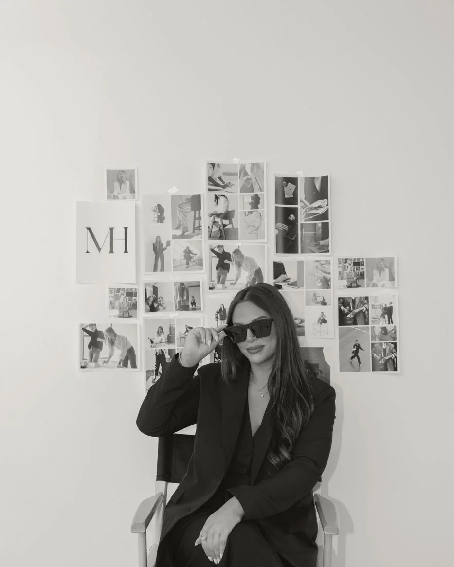 Nicole Marcus seated in front of a wall of taped photographs