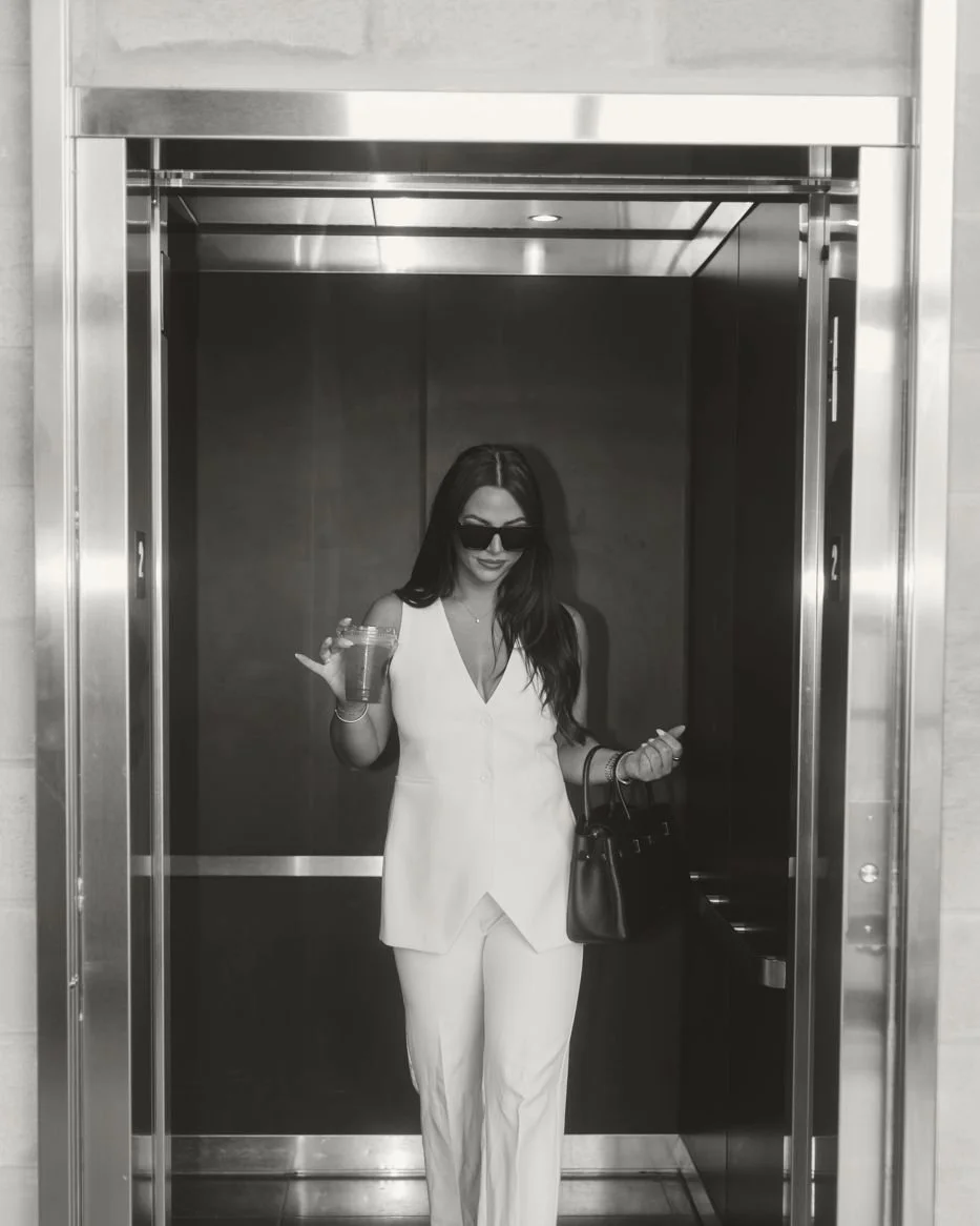 Nicole Marcus, founder of MARCETING HOUSE, in a white suit stepping out of an elevator