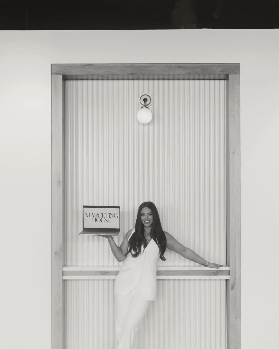 Nicole Marcus, founder of MARCETING HOUSE, in a white suit beside the MARCETING HOUSE sign