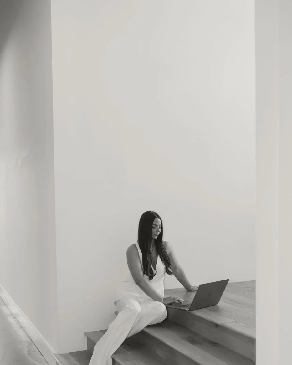 Nicole Marcus, founder of MARCETING HOUSE, working on a laptop on studio stairs