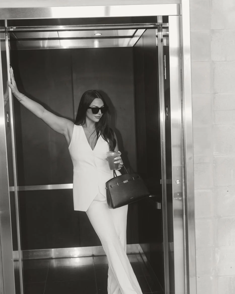 Nicole Marcus, founder of MARCETING HOUSE, in a white suit leaning in an elevator doorway