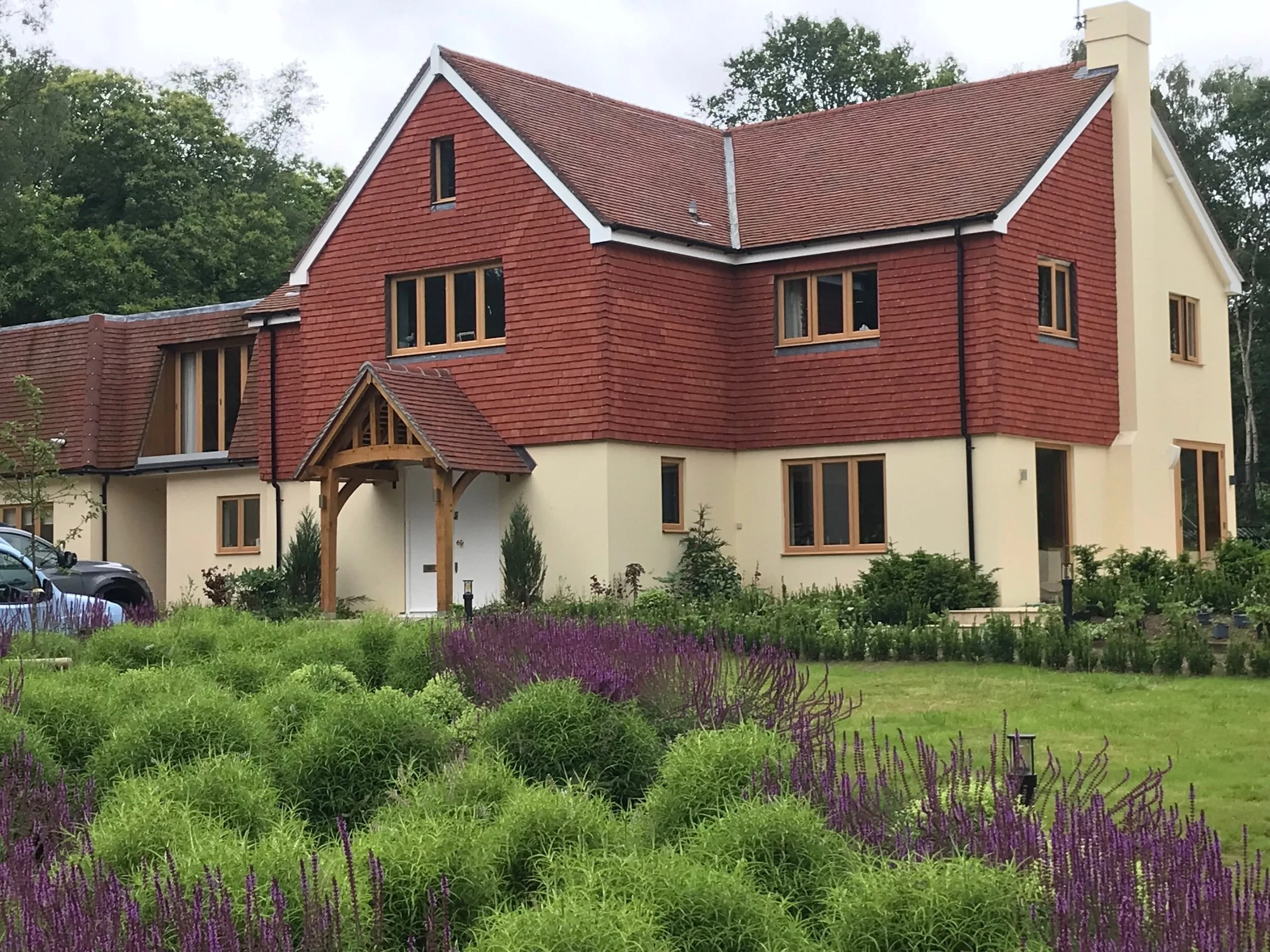 A tile-hung country house framed by flowing grasses and flowering borders at The Oaks.