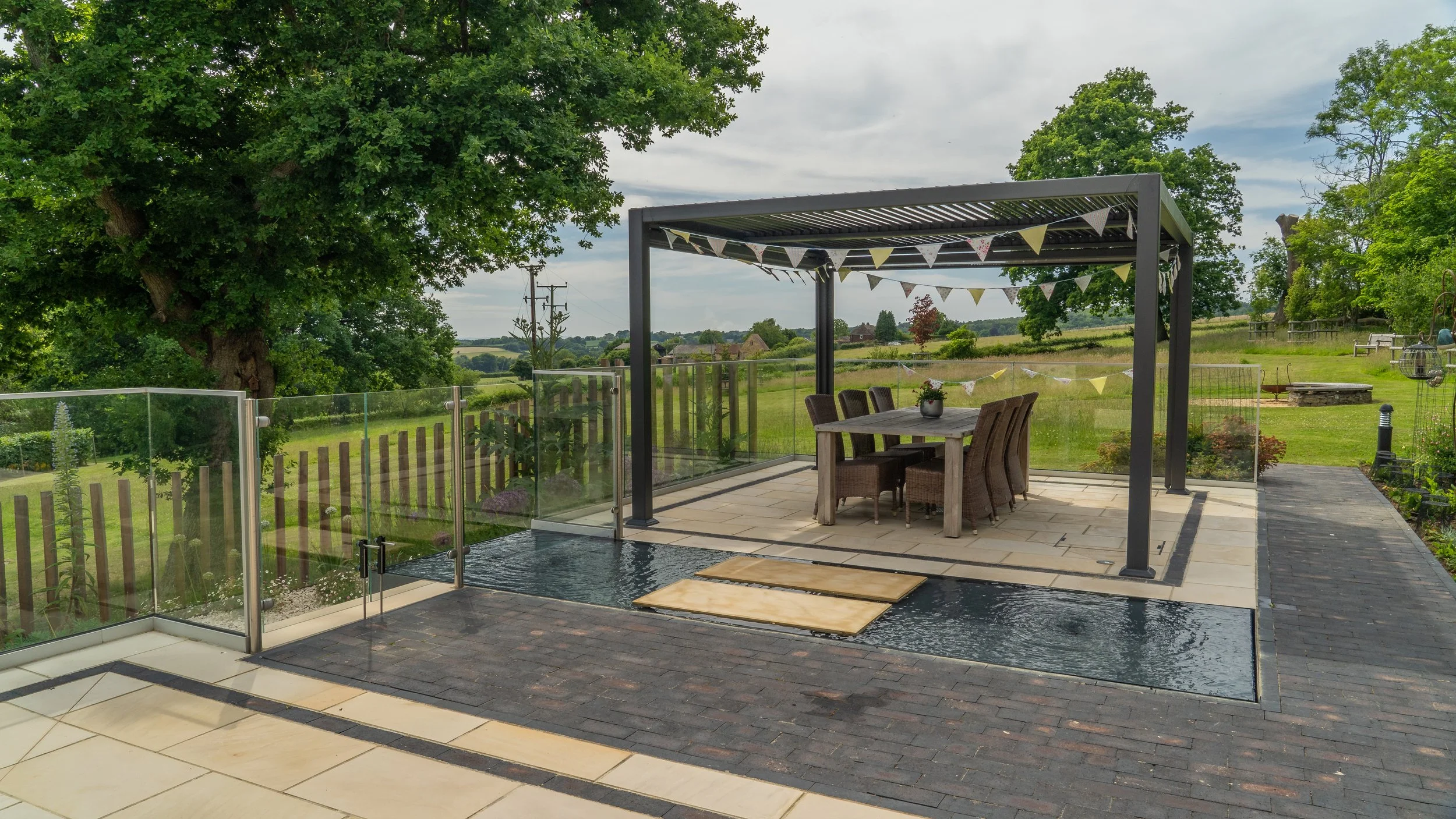 A sheltered dining terrace beside water, overlooking the wider landscape at The Paddocks.