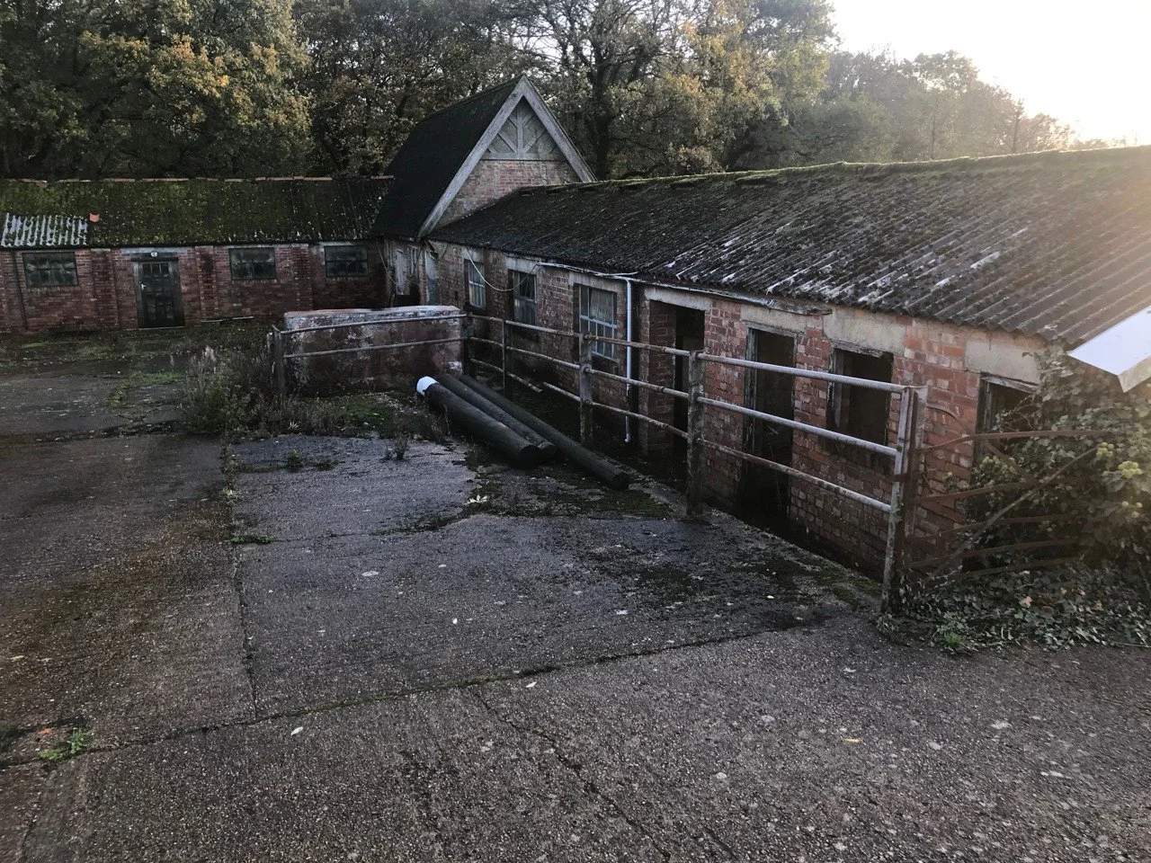Existing brick farm buildings around a worn concrete courtyard, before the proposed conversion.