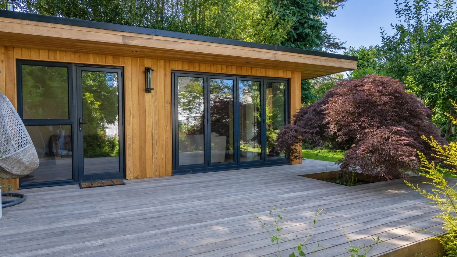 The timber garden room opens onto its deck beside established planting.