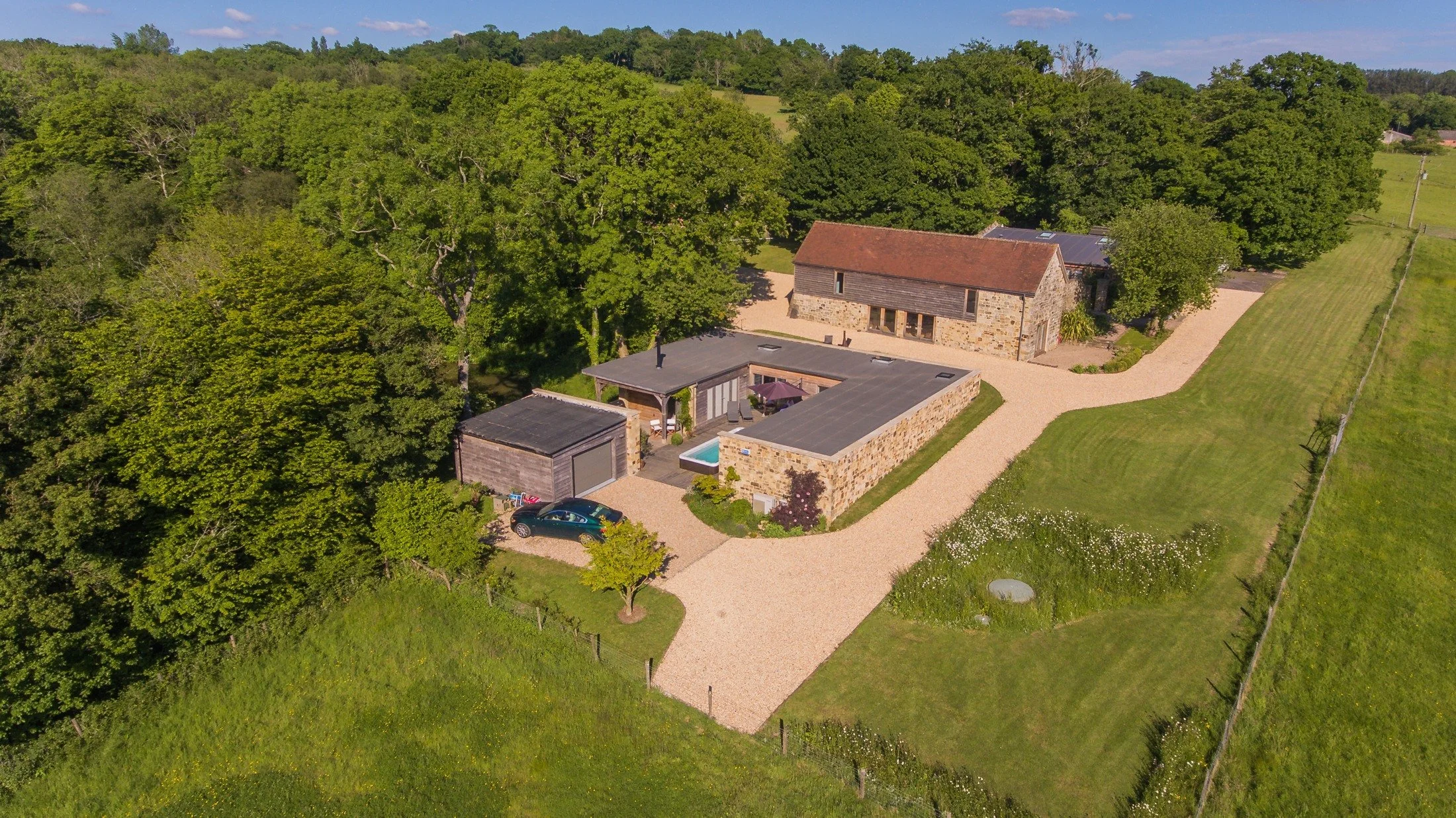 Aerial view showing the low courtyard annexe beside the main barn house, surrounded by trees and fields.