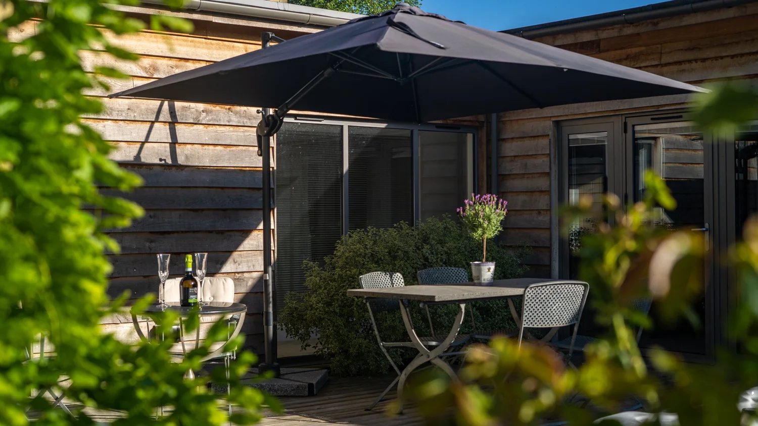 An intimate outdoor dining area under a parasol, framed by planting and timber-clad walls.