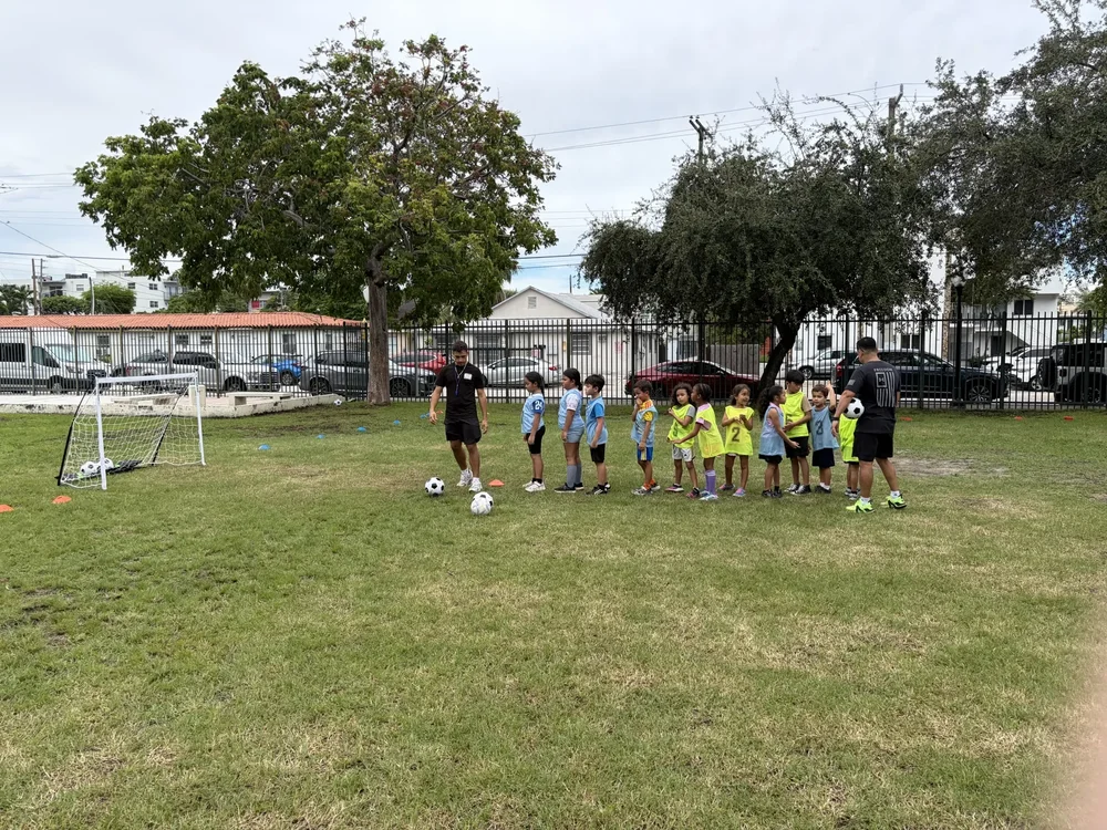 Children in blue and yellow soccer jerseys line up with two coaches on a grass field.