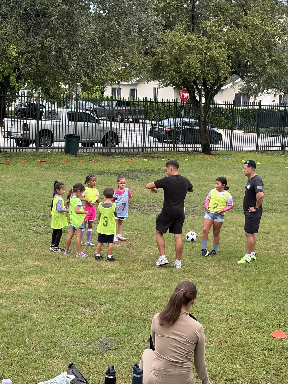 Children gather around two coaches for instructions on the soccer field.