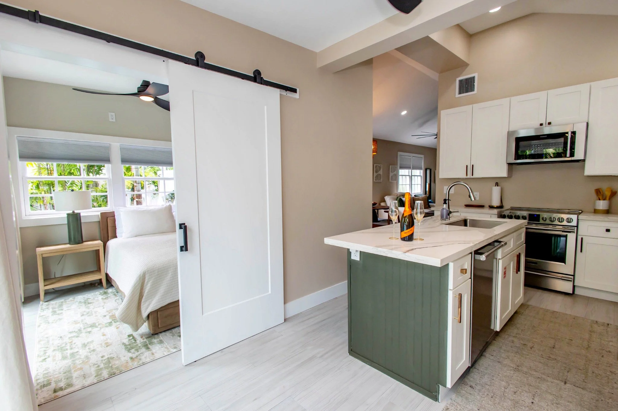 A suite with a kitchen island, wine glasses, and a bedroom in the background.