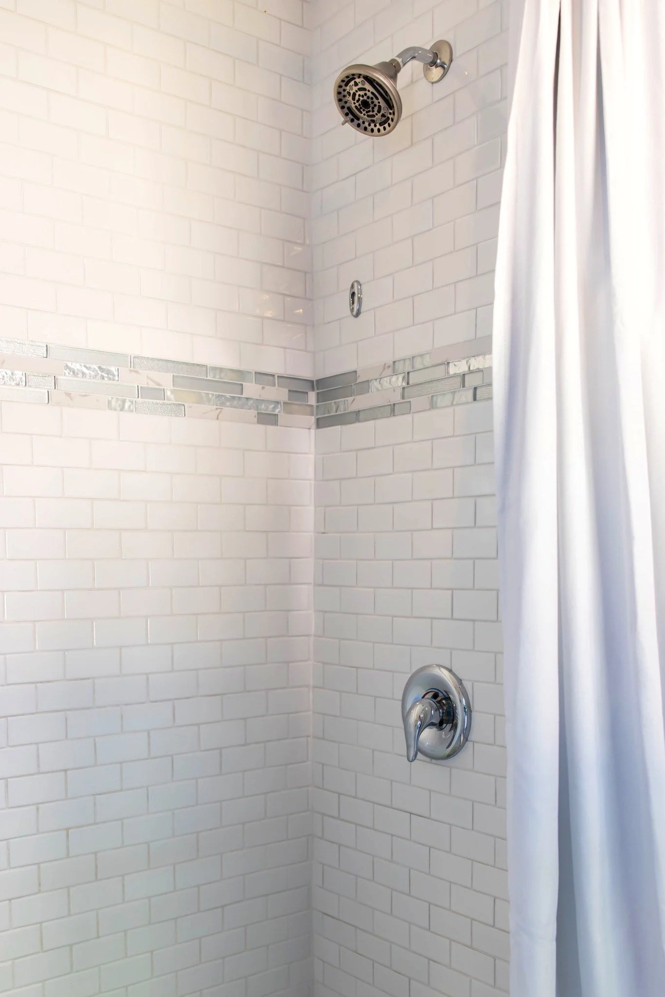 A shower with white tile walls and a silver shower head.