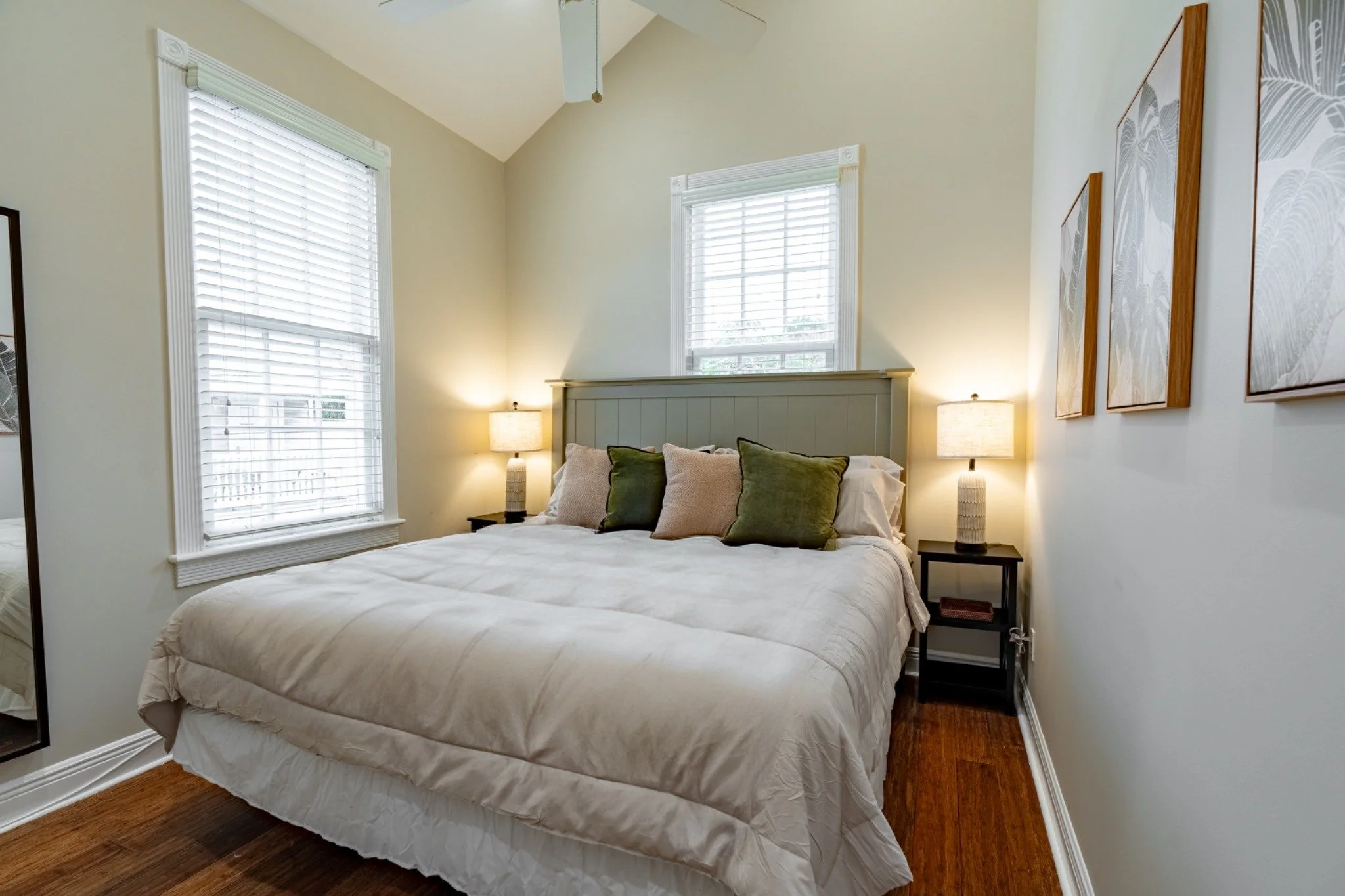 A wide-angle view of a bedroom with a large bed, two nightstands, and two windows.