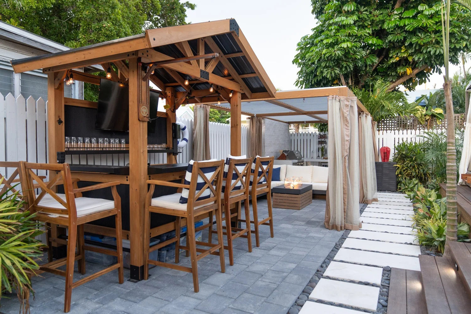 Timber outdoor bar with high stools beside the pergola