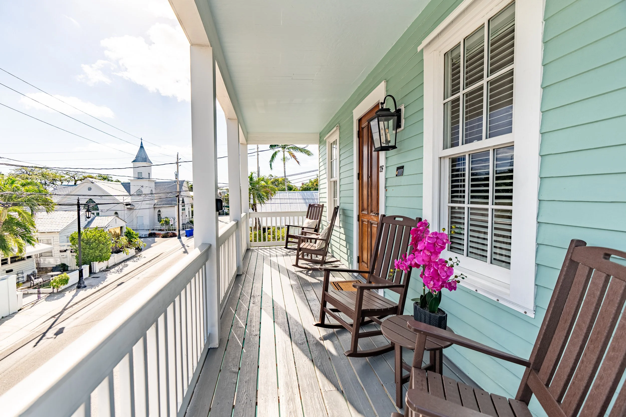 A light blue house with a porch featuring wooden rocking chairs and a pink orchid.