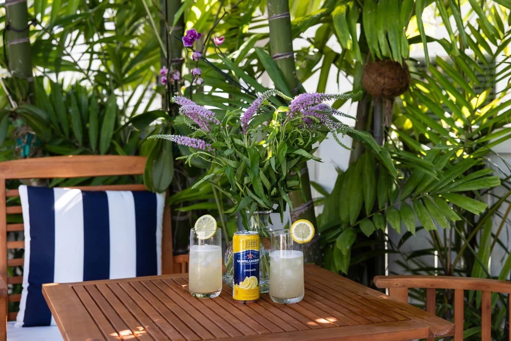 Wooden outdoor table with flowers and two drinks among tropical plants