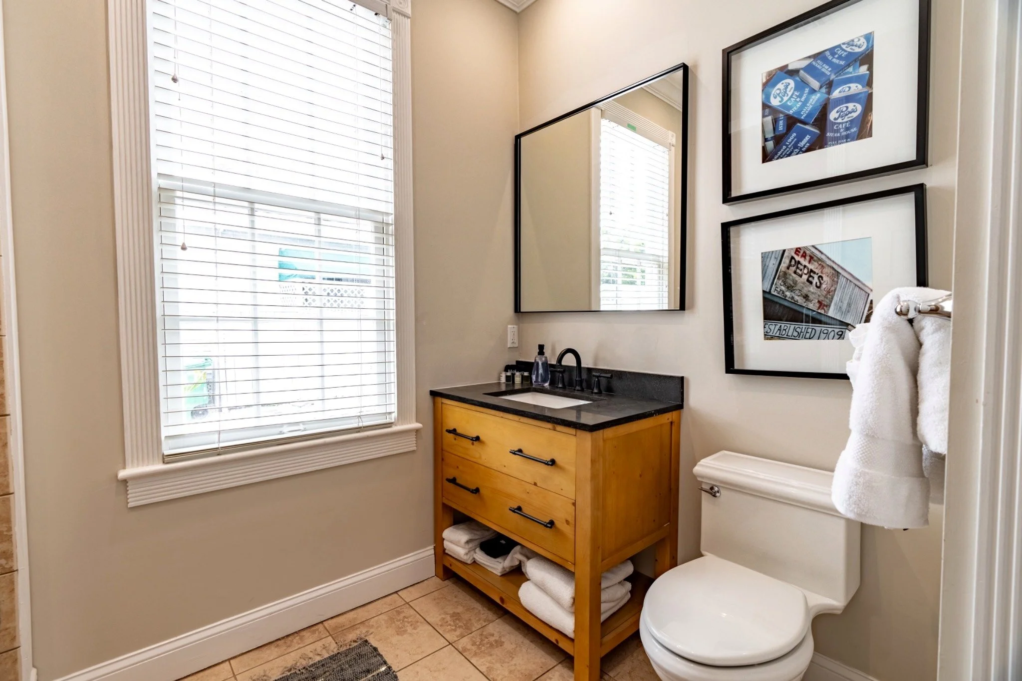 A clean and well-appointed bathroom with a wooden vanity, white toilet, and framed pictures on the wall.