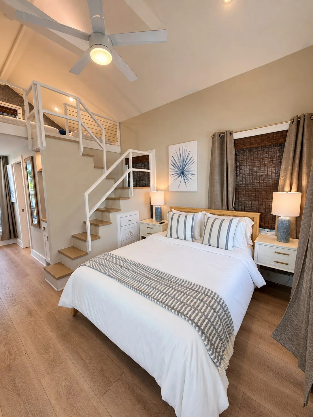 Queen bed with coastal bedding beside the loft staircase
