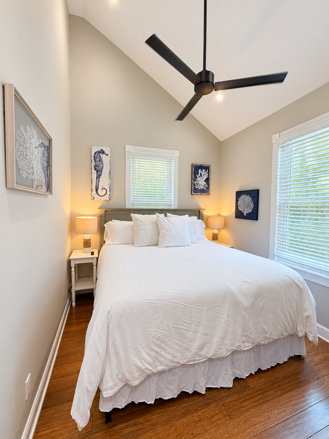 A neatly made bed with white linens in a cozy room with vaulted ceiling, wooden floor, and nautical-themed artwork.